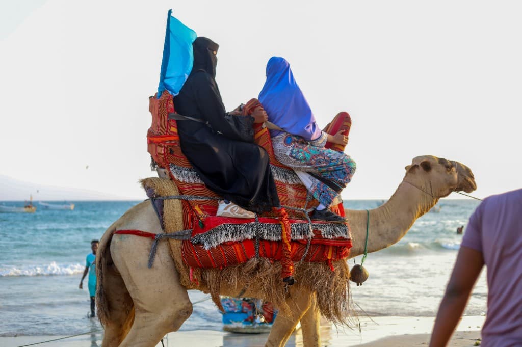 Women riding a camel along a scenic beach